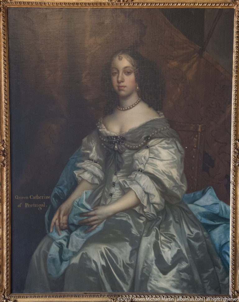 Seated portrait of Queen Catherine of Portugal in a silver-gray gown with pearls and blue drapery against a dark interior.