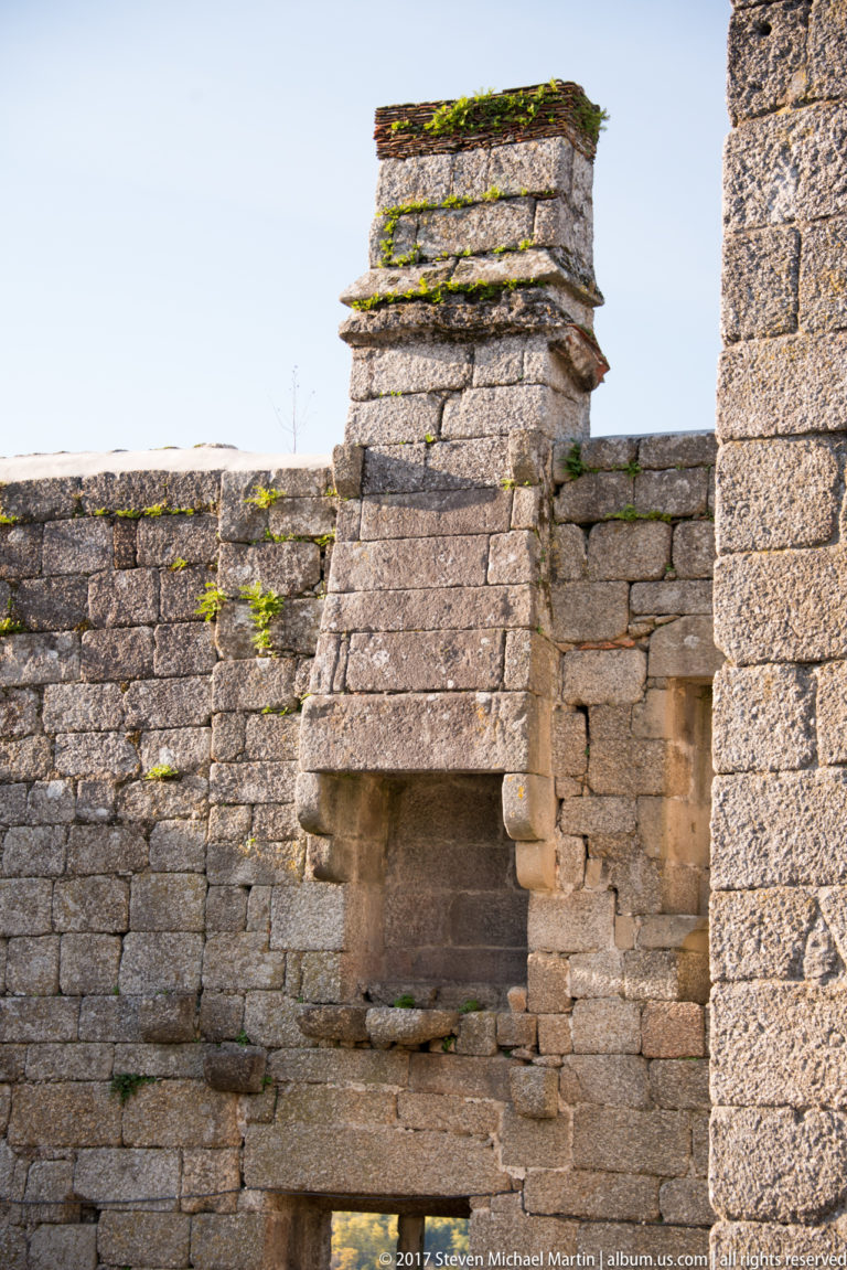 Large projecting stone fireplace with broad hood, corbel supports, and moss on the upper masonry inside Guimarães Castle.
