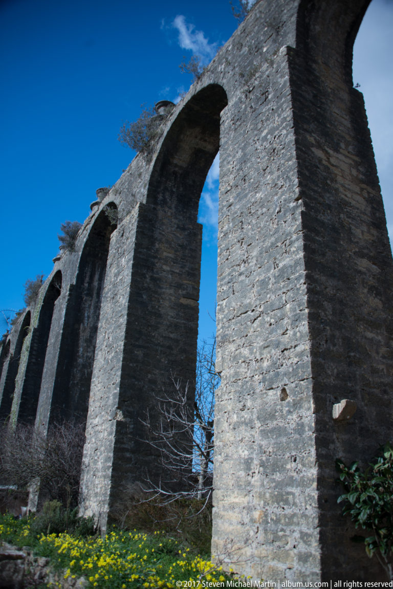 Tall stone arches and massive piers of the Pegões Aqueduct viewed from ground level near Tomar.