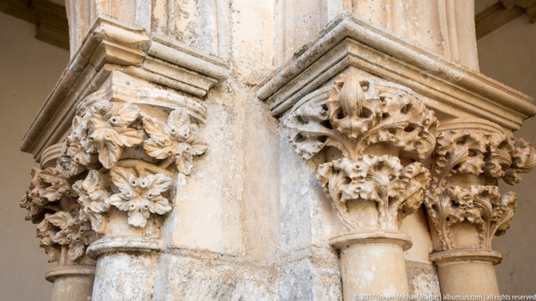 Clustered pale stone capitals carved with dense foliage and mask-like grotesque faces on adjoining columns.