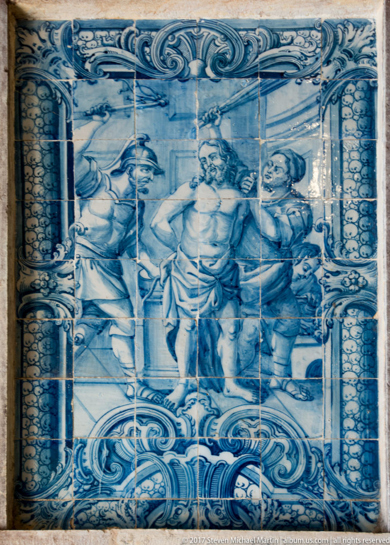 Blue-and-white ceramic tile panel showing three male figures framed by painted columns and scrolling ornamental borders.