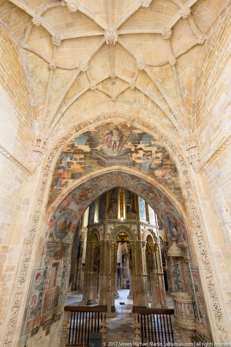 Wide interior view beneath pale ribbed vaulting through a painted arch toward the gilded central structure of the Charola.