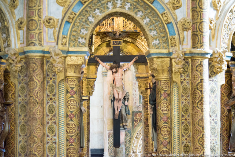 Crucified Christ on a dark cross marked INRI, centered within a richly painted and gilded architectural surround.