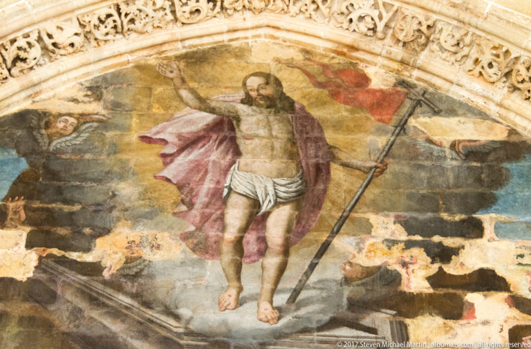 Painted resurrected Christ standing above a tomb with raised hand, red mantle, halo, and long cross-staff.