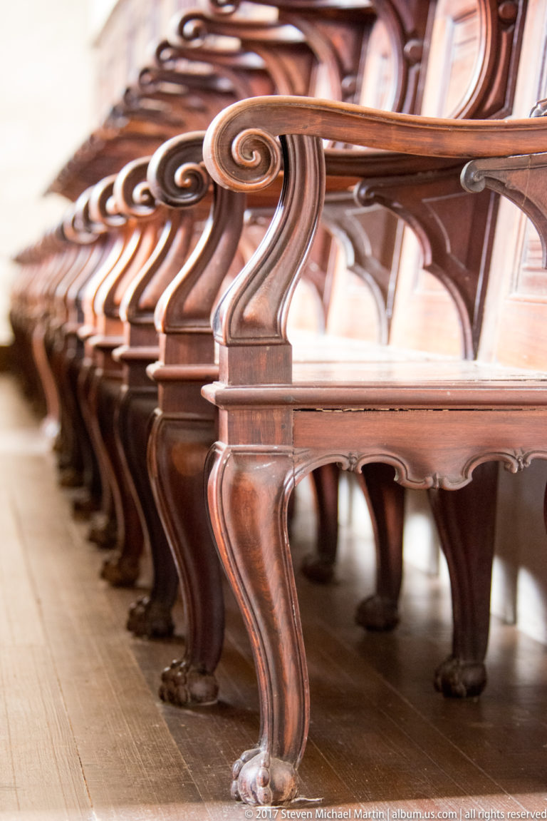Low-angle close view along a row of polished wooden church seats with repeated curved arm supports and carved feet.
