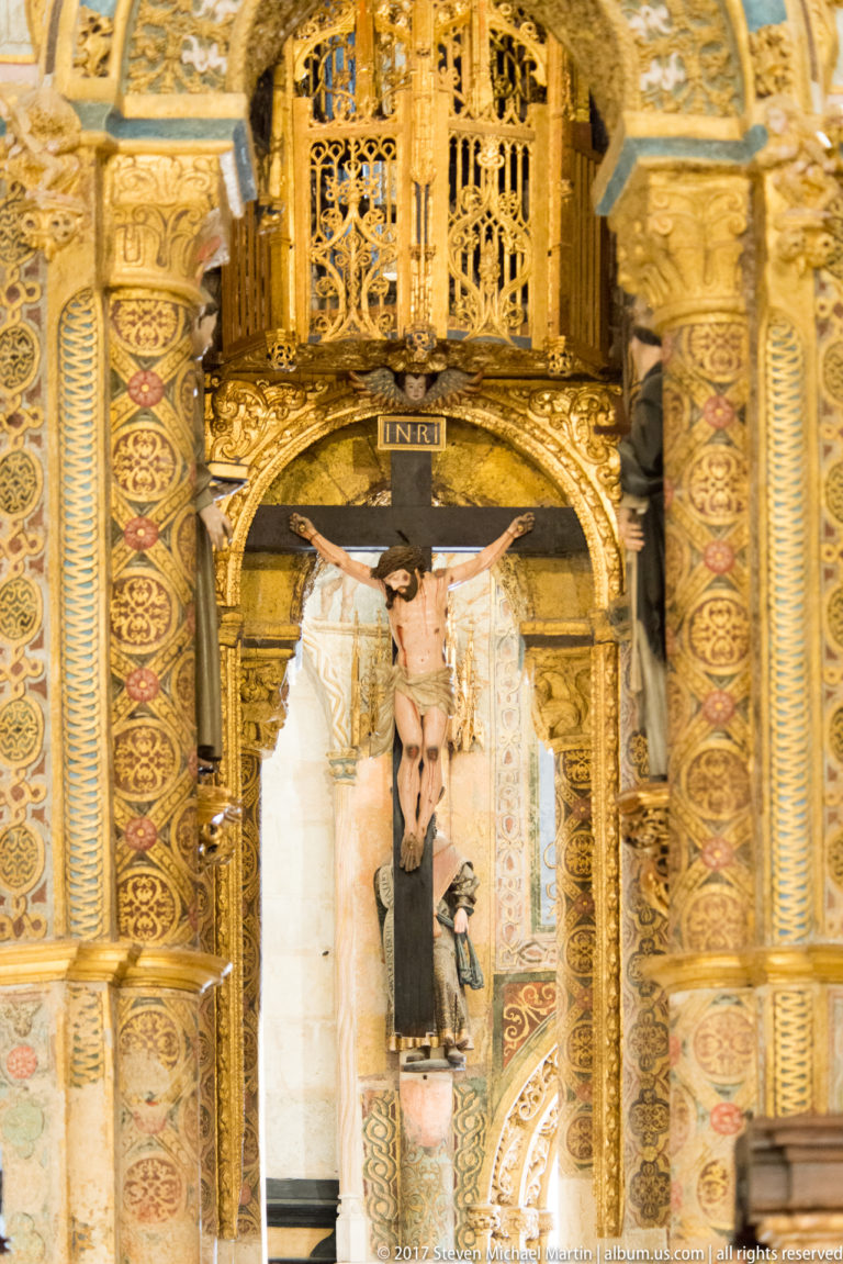 Gilded and painted arch, patterned columns, carved screen, and devotional figure inside the Charola at Tomar.