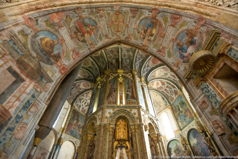 Broad painted arch filled with figural scenes frames the gilded central core of the Charola; a carved projection appears at right.