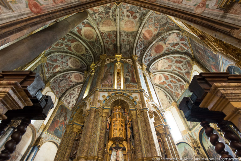 Charola central core beneath painted vaults, framed in the foreground by dark wooden choir or church furnishings.