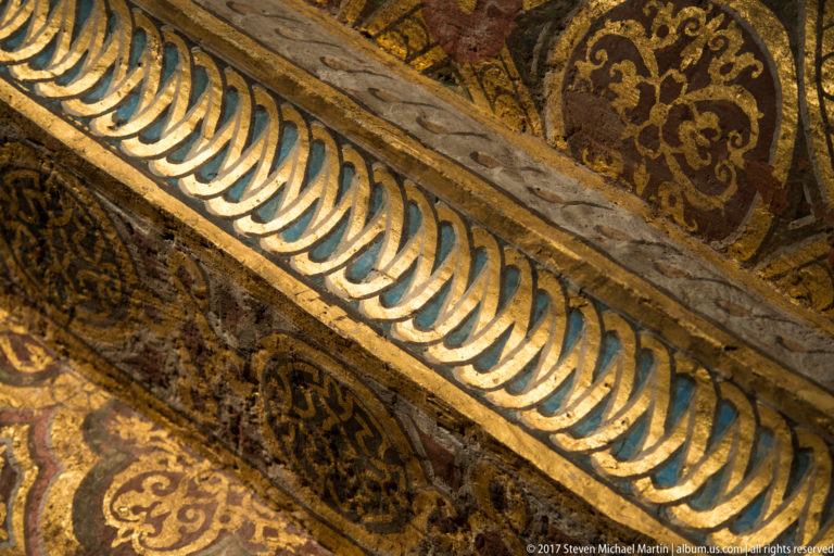 Diagonal interior molding with repeating blue-and-gold leaf shapes between red-and-gold painted decorative panels.