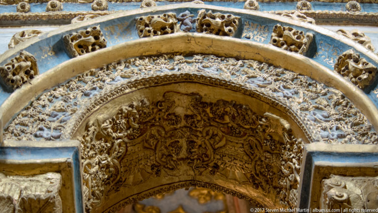 Close view of an interior arch covered in gilded relief, blue painted bands, and dense ornamental patterns.