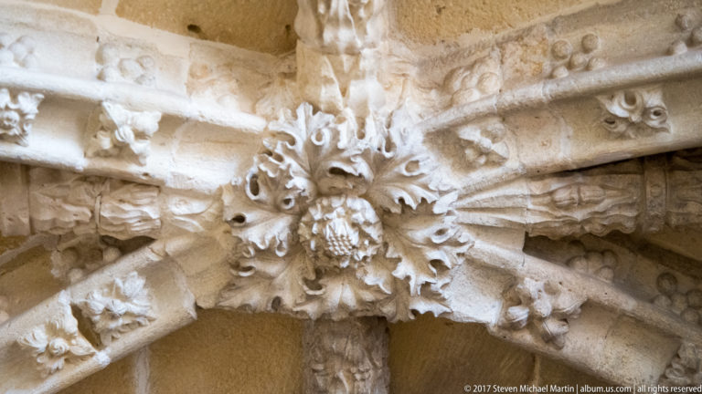 Carved stone vault boss with radiating ribs and dense foliate ornament in pale limestone.