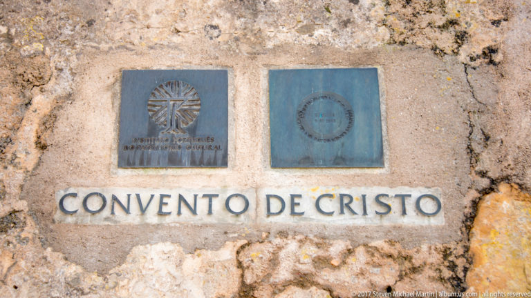 Two metal heritage plaques mounted above the carved words “CONVENTO DE CRISTO” on a rough stone wall.