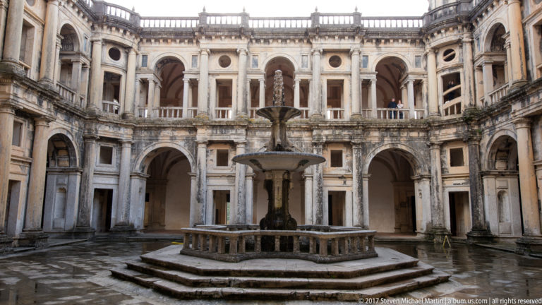 Symmetrical Renaissance cloister court with two-story arcades surrounding a central tiered fountain on an octagonal stepped base.