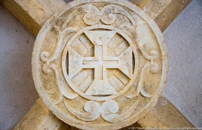 Circular stone medallion with a carved cross and scrolling foliage at the intersection of diagonal architectural ribs.