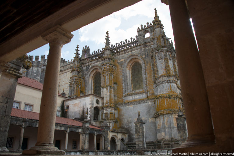 Ornate church elevation with tall arched windows and pinnacles, framed by columns of a cloister arcade.