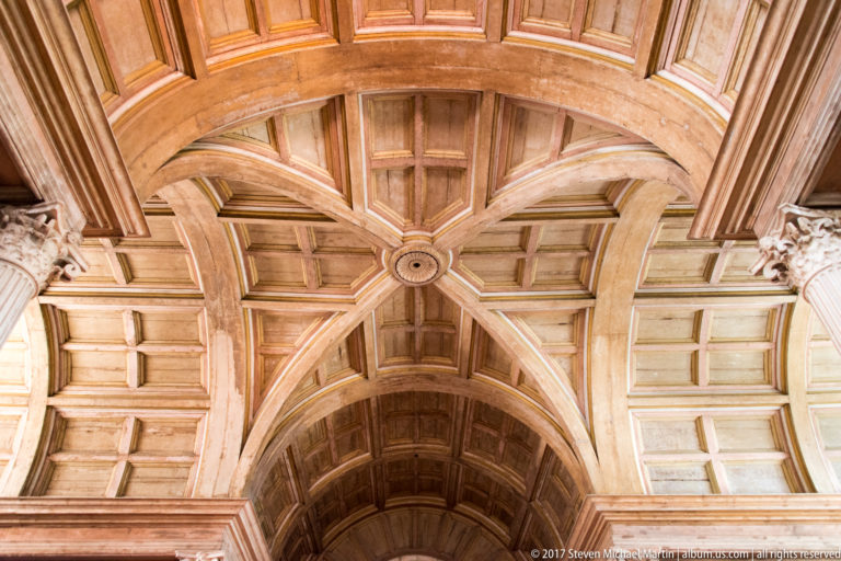 Warm wooden coffered ceiling with intersecting molded ribs, a circular central boss, and curved paneled bays.