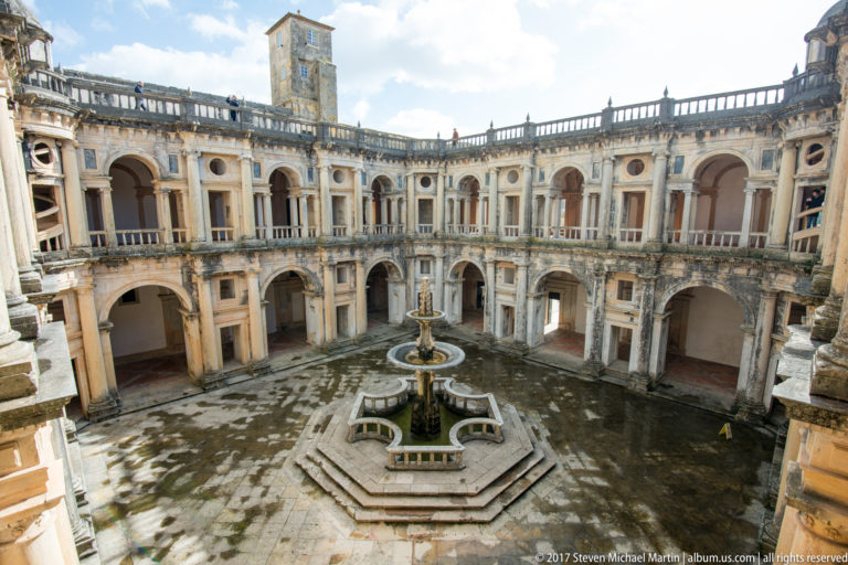 Wide upper-level view of the Cloister of John III with two-story arcades, central fountain, and square tower.
