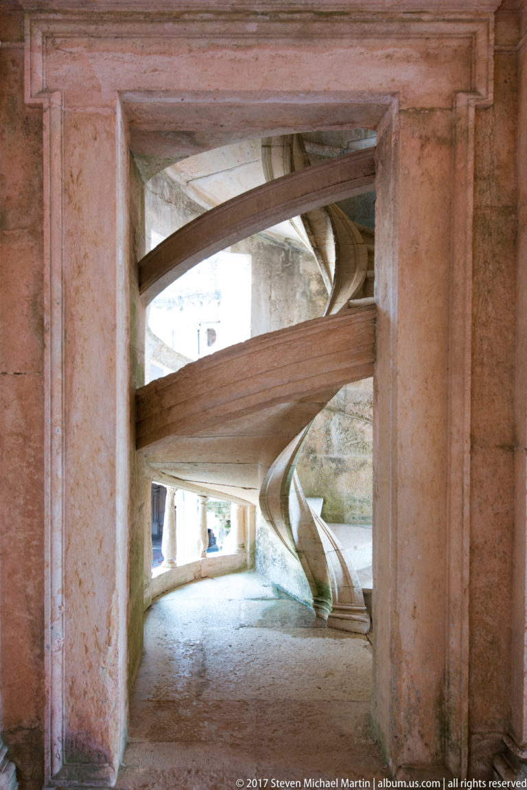 Stone spiral staircase seen through a rectangular opening, with curved treads and underside crossing the passage.