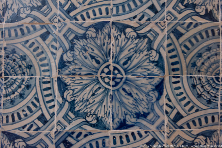 Blue-and-white azulejo tiles forming large radial flowers, scrolling leaves, circles, and geometric bands.