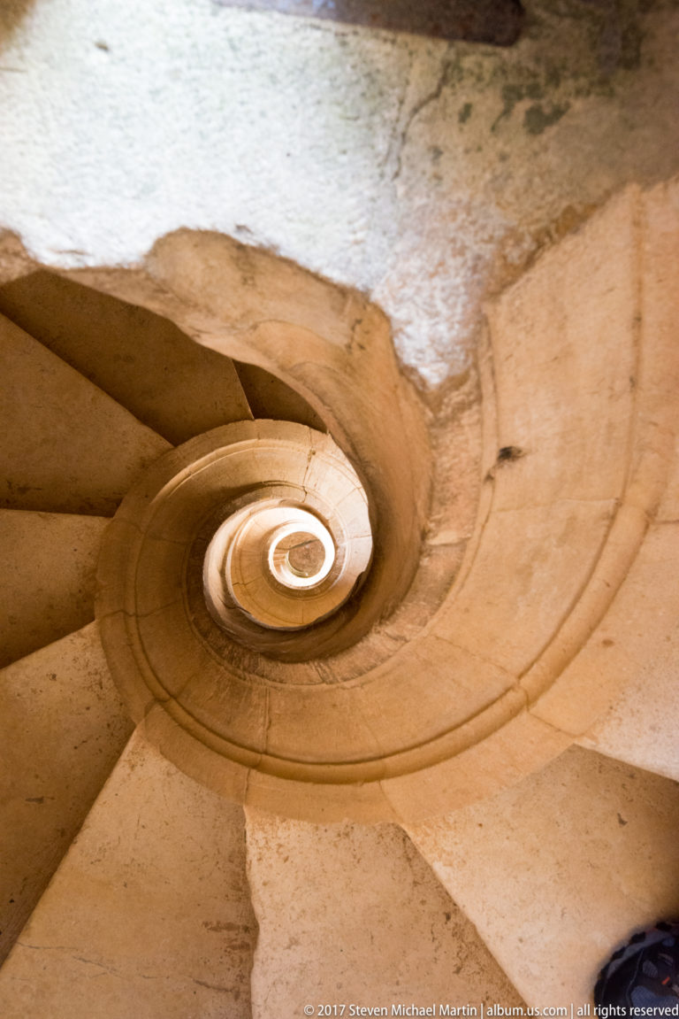 Underside of a pale stone spiral staircase curling upward in a tight coil at the Convent of Christ.