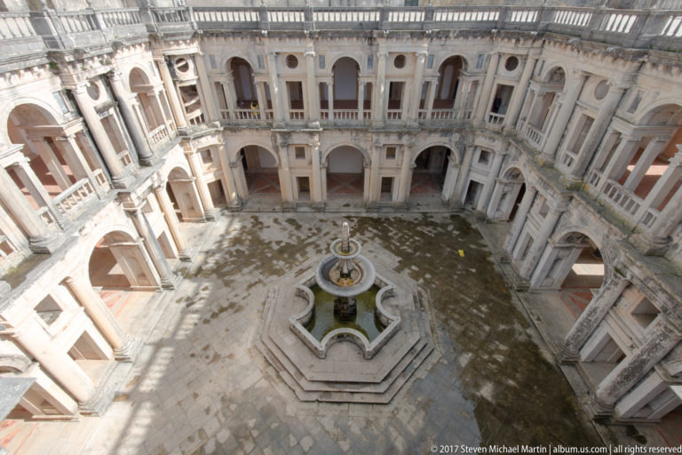 High view into the Cloister of John III, with two-story arcades surrounding an octagonal fountain and paved court.