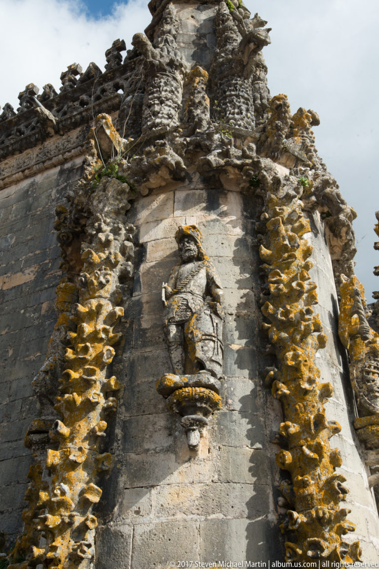 Weathered stone figure in a niche surrounded by dense carved ornament on an exterior wall at Tomar.