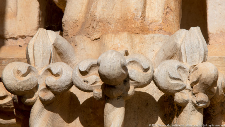 Close-up of a row of projecting floral stone carvings with curled leaves and deep sunlit shadows.