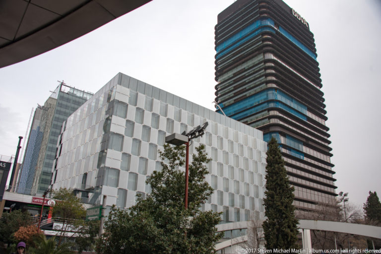 White modern building with repeating geometric façade in front of a tall dark horizontally banded tower in Madrid.
