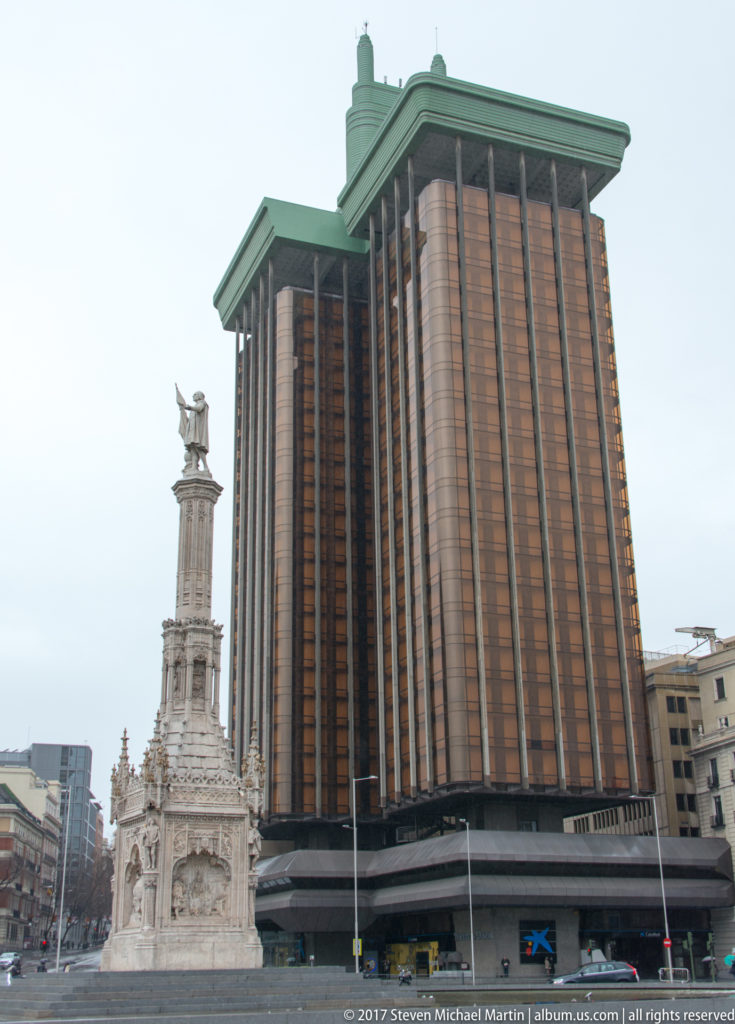 Monument to Columbus beside the tall copper-toned Torres de Colón and surrounding buildings at Plaza de Colón.