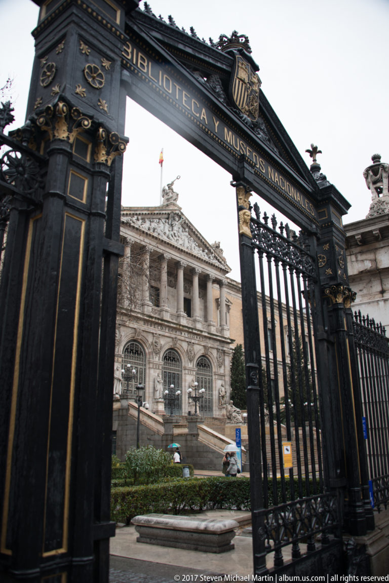 Black and gilded iron gate reading “BIBLIOTECA Y MUSEOS NACIONALES,” framing the National Library façade beyond.