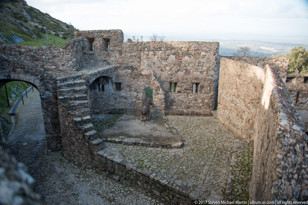 Stone courtyard with cobbled paving, stairs, arches, and narrow wall openings inside Marvão Castle.