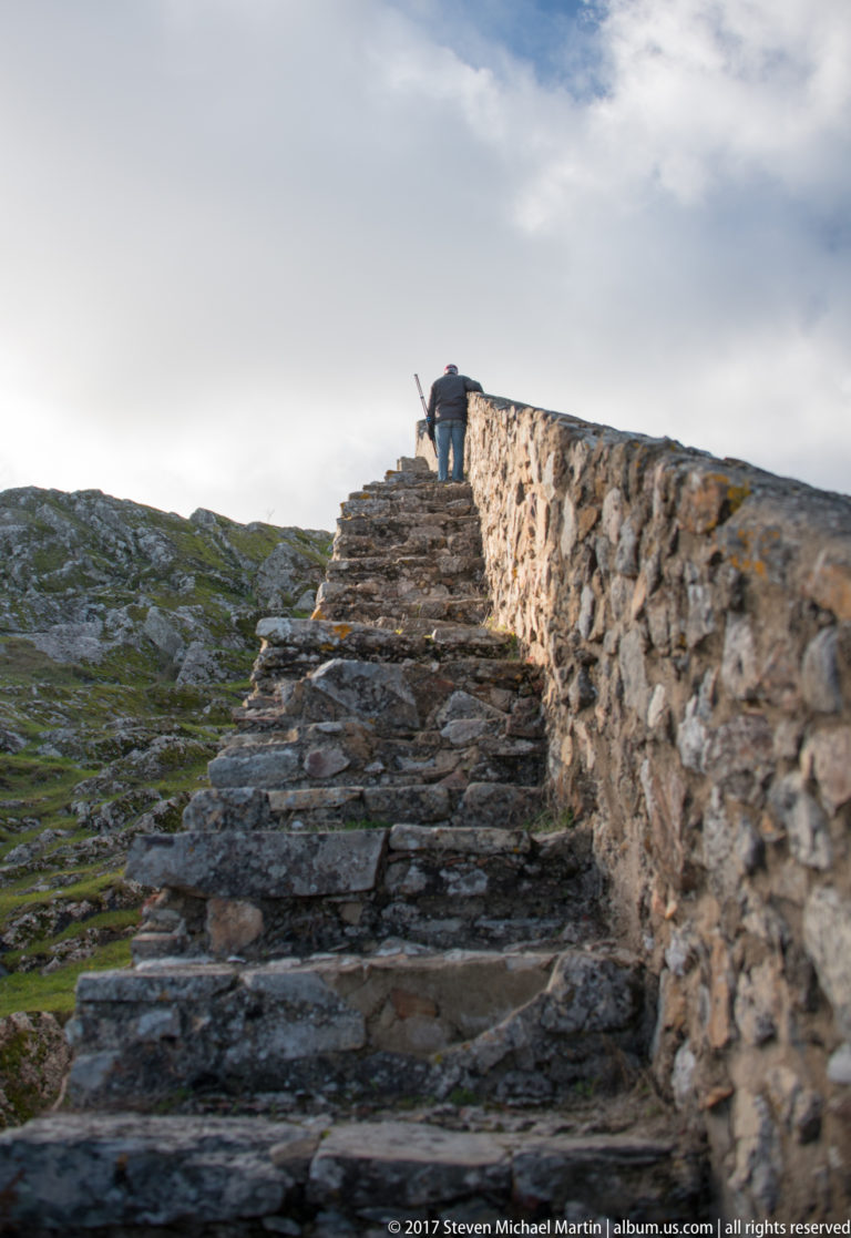 Rough stone steps climb beside a low fortification wall toward a visitor on Marvão’s rocky summit.