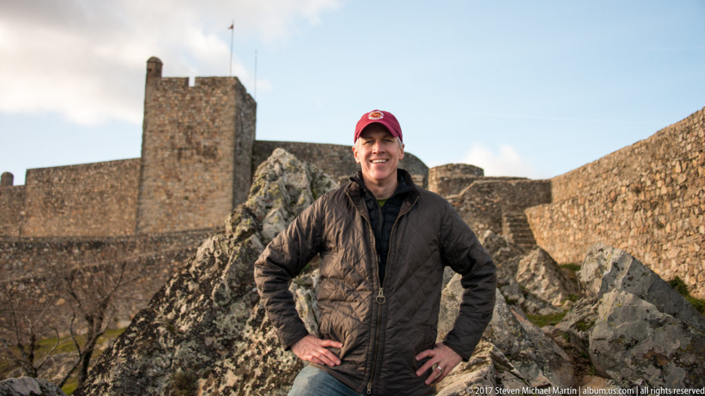 Smiling visitor in a red cap stands on rocky ground before Marvão Castle’s keep and walls.