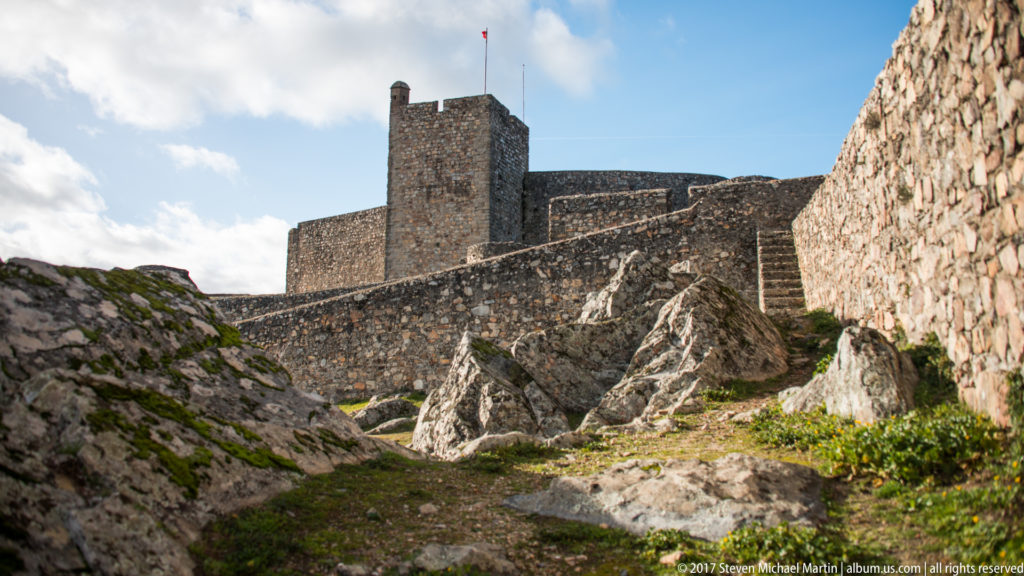 Square keep and layered stone walls of Marvão Castle rise above jagged bedrock under a blue sky.