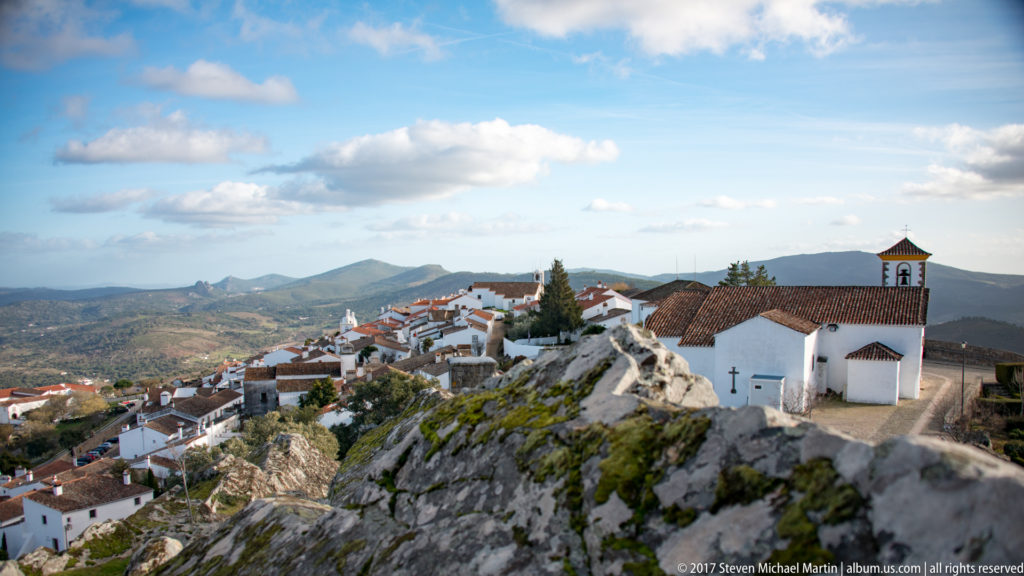 White houses and a small church cluster across Marvão’s rocky summit above a broad mountain landscape.