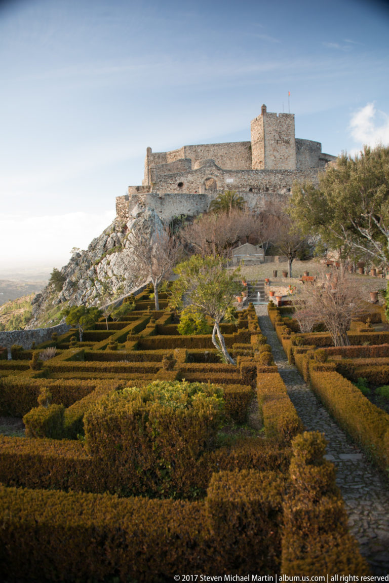 Rectangular clipped hedges and paths in a formal garden with Marvão Castle and its square keep on the ridge beyond.