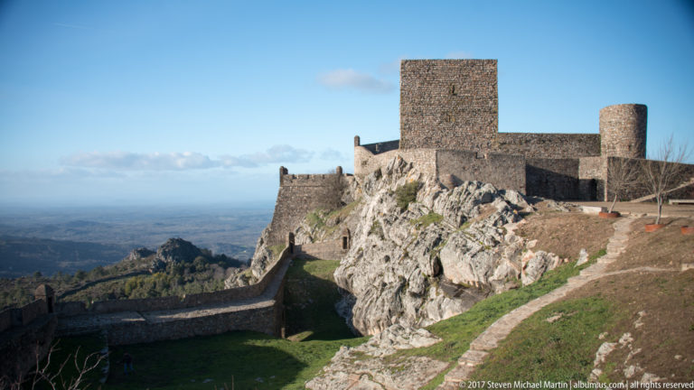 Broad view of Marvão Castle keep and round tower above granite, with lower walls enclosing a grassy hollow.