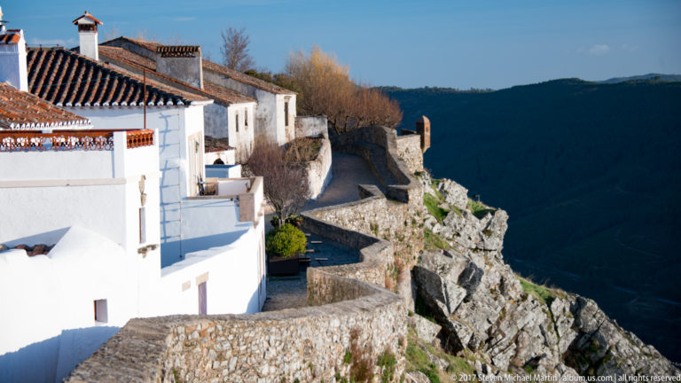 White houses and a narrow paved route follow stone walls along Marvão’s rocky cliff above a deep valley.