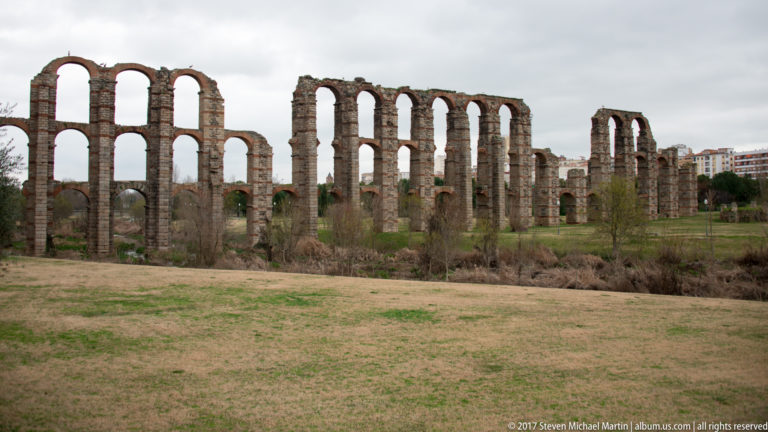 Freestanding sections of Mérida's Acueducto de los Milagros with tall stacked arches rising from an open grassy field.