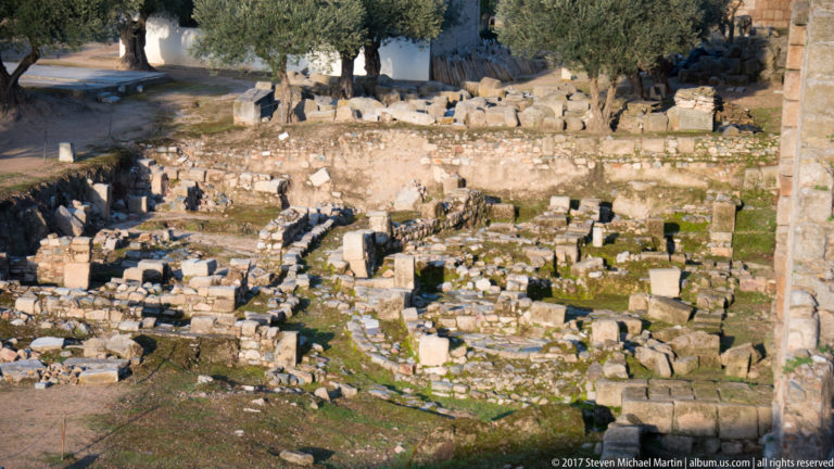 Dense excavated stone walls, blocks, and channels with patches of moss beneath olive trees.