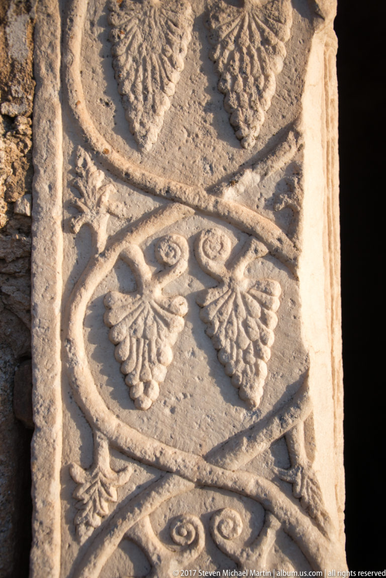 Close-up of a weathered stone panel carved with repeating leaves, scrolls, and intersecting bands.
