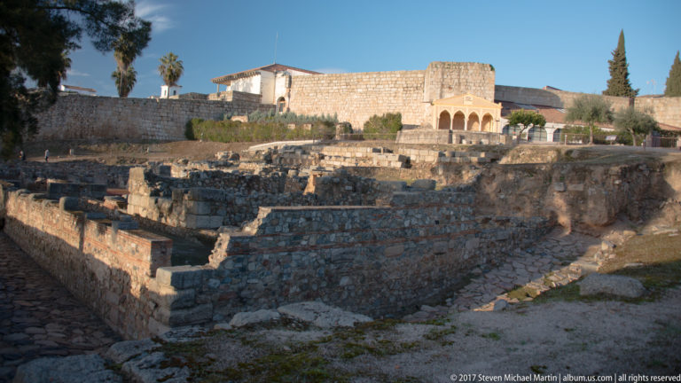 Terraced excavated stone and brick walls with a small arcade and fortified wall in the background.