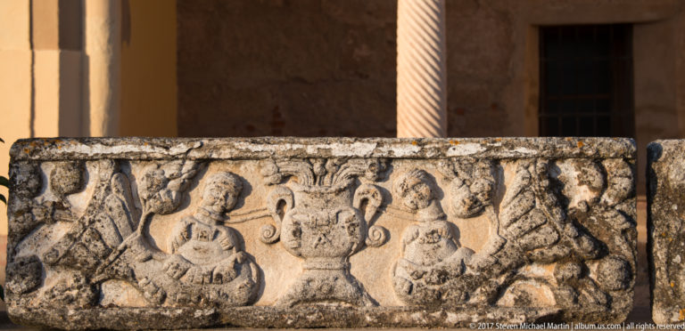 Weathered rectangular relief with a central handled vessel, paired human figures, and worn decorative motifs.