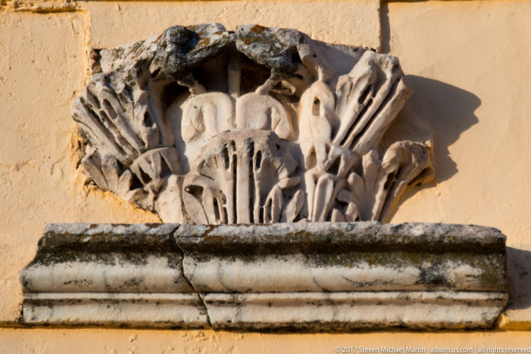 Close-up of a weathered carved capital with layered acanthus-like leaves mounted above a molded base.