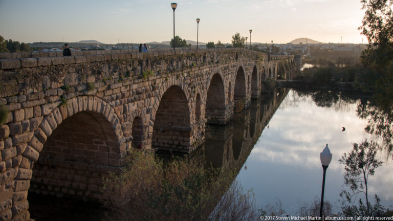 Oblique view along Mérida's Roman bridge, with repeated stone arches reflected in the calm Guadiana River.