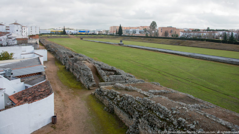 Elevated view across long masonry remains and lawns of Mérida's Roman circus, with modern buildings beyond.