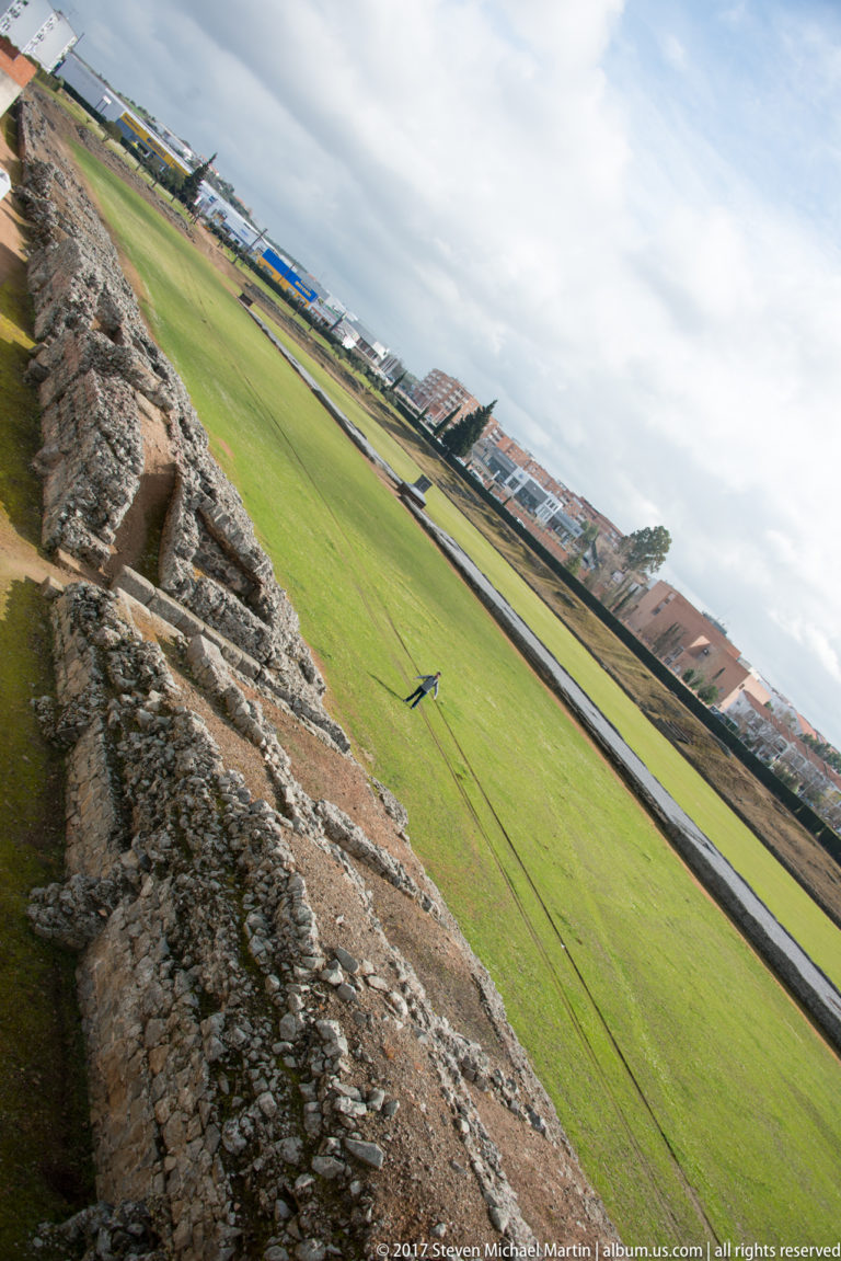 Rough archaeological masonry in foreground overlooking the broad grassy track and central remains of Mérida's Roman circus.