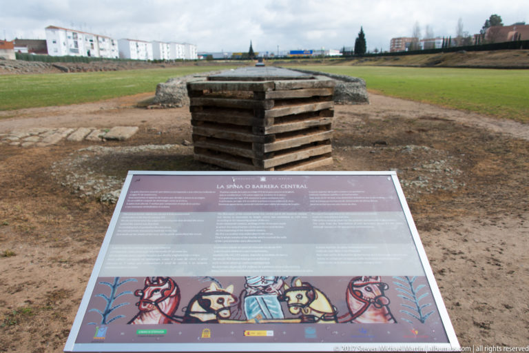 Interpretive panel about the central arena barrier positioned before low archaeological remains in Mérida's Roman circus.