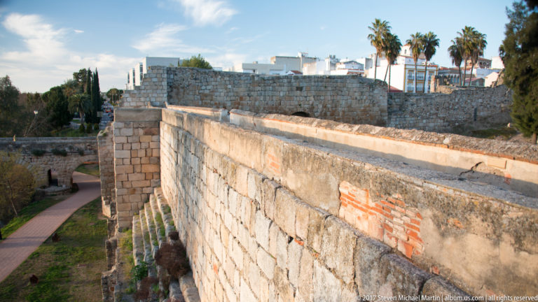 Oblique view along a massive squared-stone wall with brick repairs and a path far below.