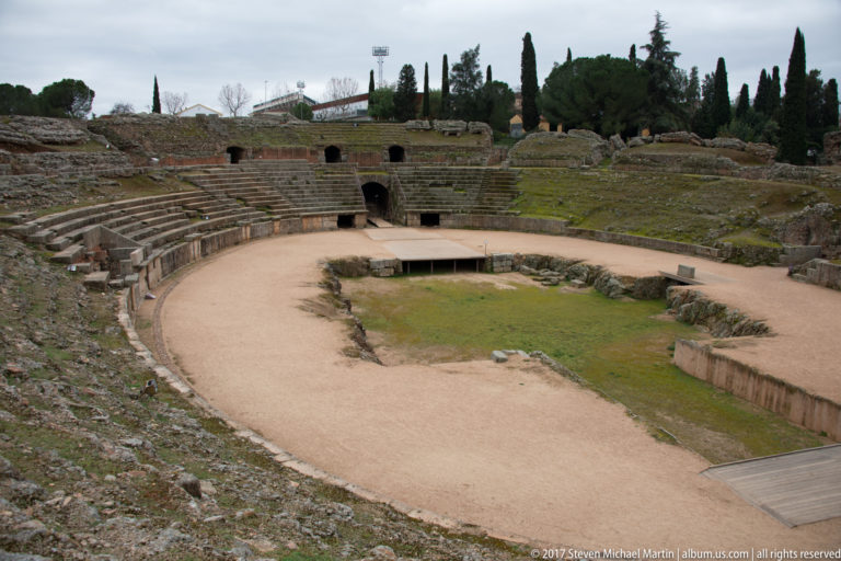 Elevated view into Mérida's Roman amphitheatre with elliptical arena, curved stone seating, and vaulted entrances.